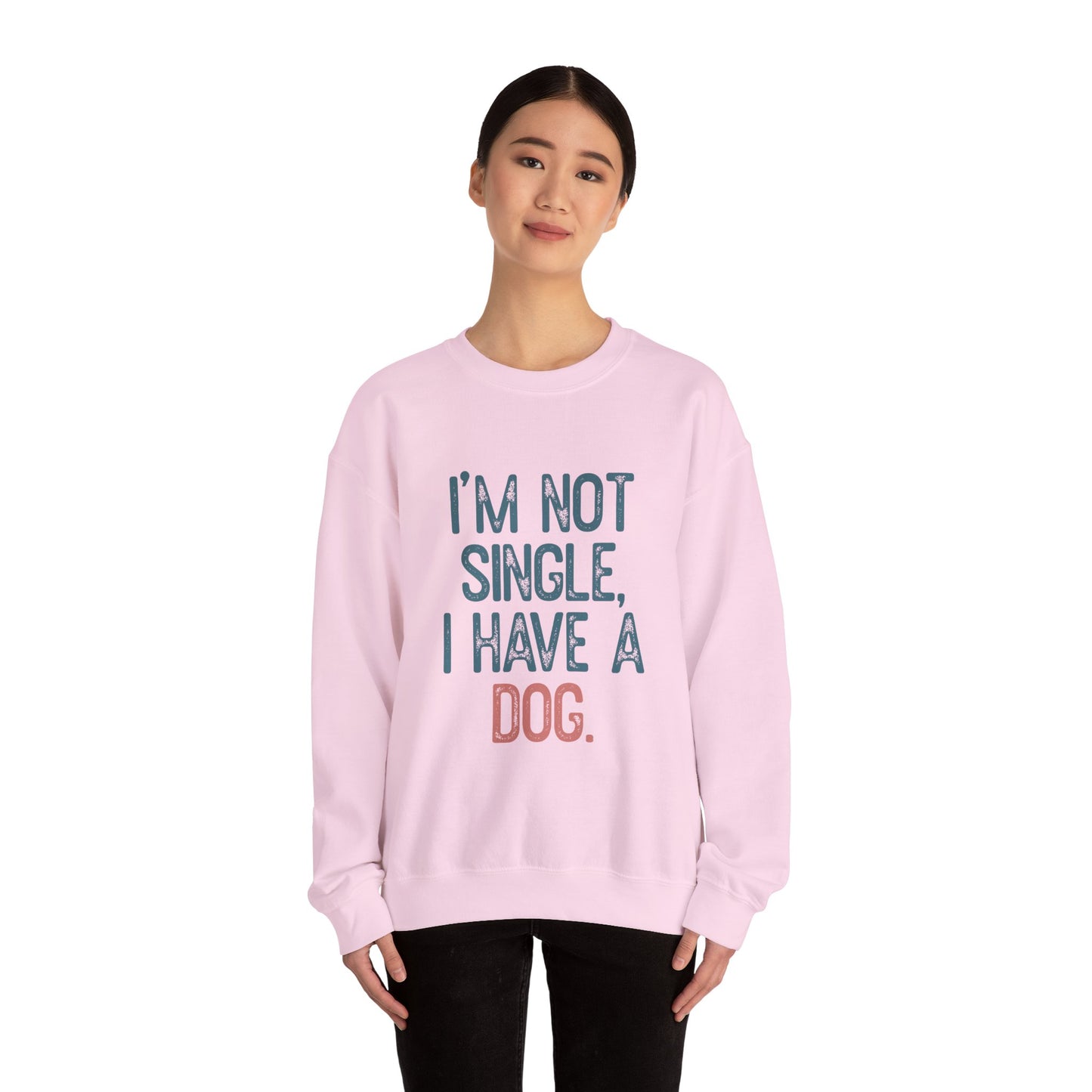 A person wears a light pink Dog Lover Crewneck Sweatshirt - I’m Not Single by Banks + Cove. With dark hair and a neutral expression, they pose against a white backdrop—a perfect gift for pet owners.