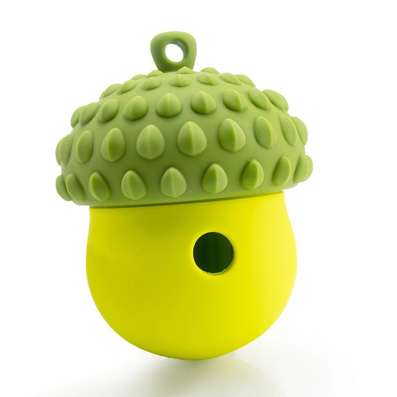 The Banks + Cove Barkorn is a green and yellow silicone acorn-shaped treat-dispensing dog enrichment toy with a textured cap, small top loop, and round hole in the yellow base, shown against a white background.