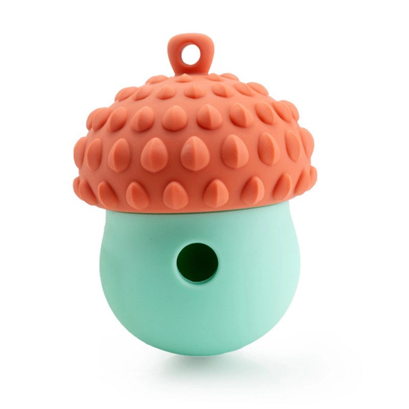 The Banks + Cove Barkorn is a silicone acorn-shaped treat-dispensing dog enrichment toy with a textured orange cap, smooth mint-green base, top handle, and circular opening for mental stimulation.