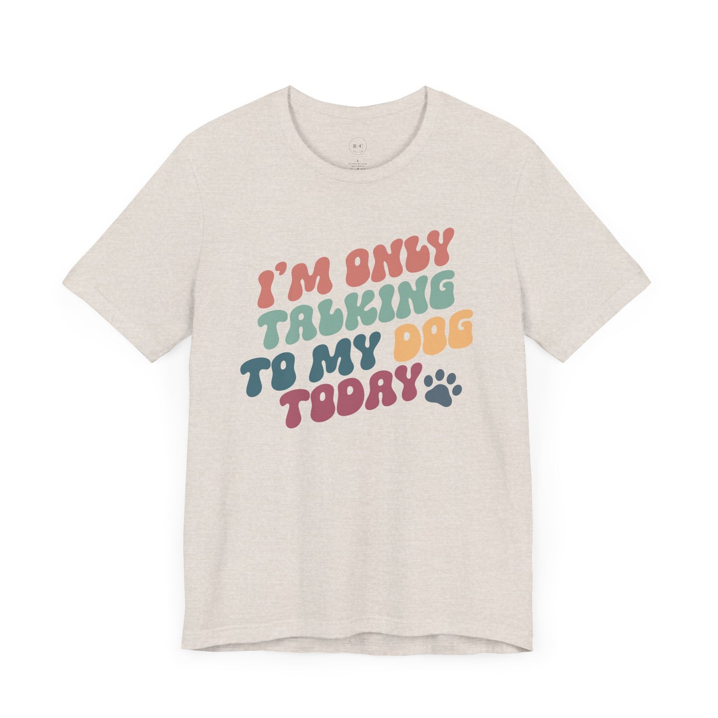 The Banks + Cove Funny Dog Lover Tee is a light beige unisex shirt featuring the colorful text Im Only Talking to My Dog Today with a small paw print. Ideal for dog enthusiasts, its perfect as a gift or for casual walks.