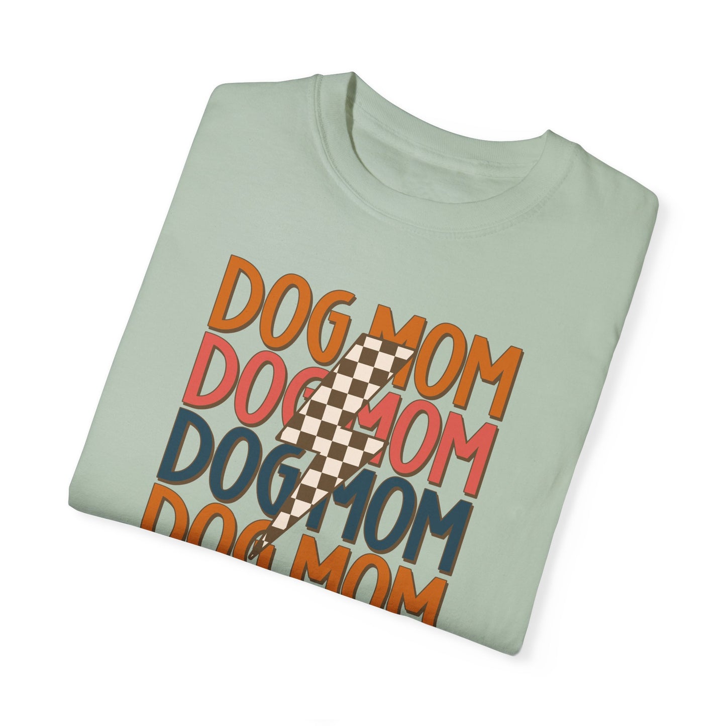 The folded Checkered Vibes Dog Mom Tee by Banks + Cove is a sage green shirt featuring DOG MOM in red, orange, and teal. A checkered lightning bolt adds retro flair, perfect for trendy dog moms exuding Dog Mom Energy.