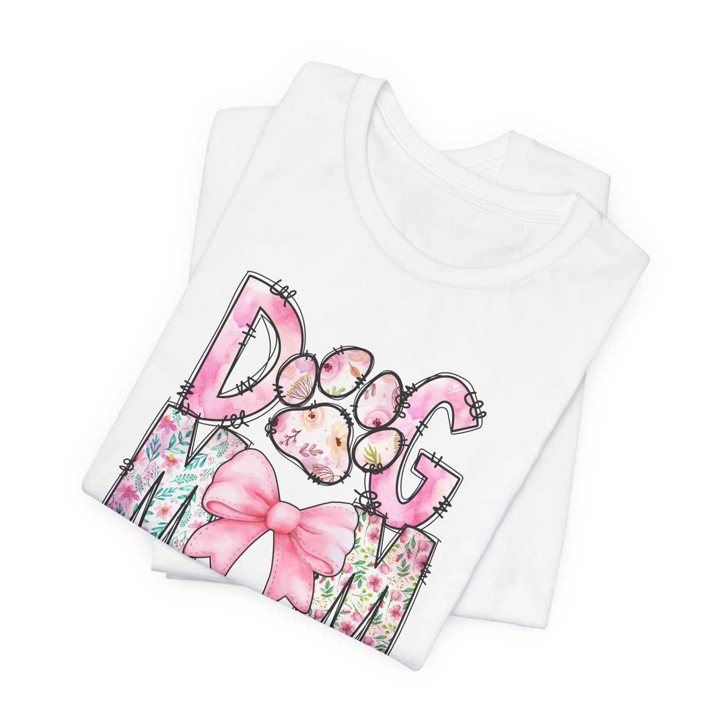 The Paws & Petals Dog Mom T-Shirt by Banks + Cove features a dogs face inside a paw print, framed with watercolor florals and a pink bow, showcasing the vibrant Paws & Petals motif on a folded white t-shirt.