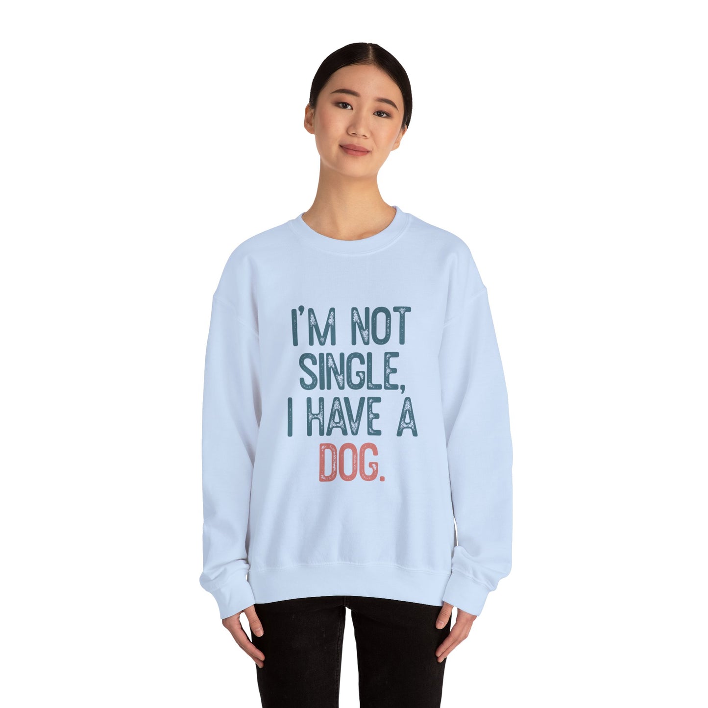 A person with a neutral expression wears the light blue Printify Dog Lover Crewneck Sweatshirt stating, IM NOT SINGLE, I HAVE A DOG. Perfect for any dog lover, the scene features their dark hair styled back against a plain white background.