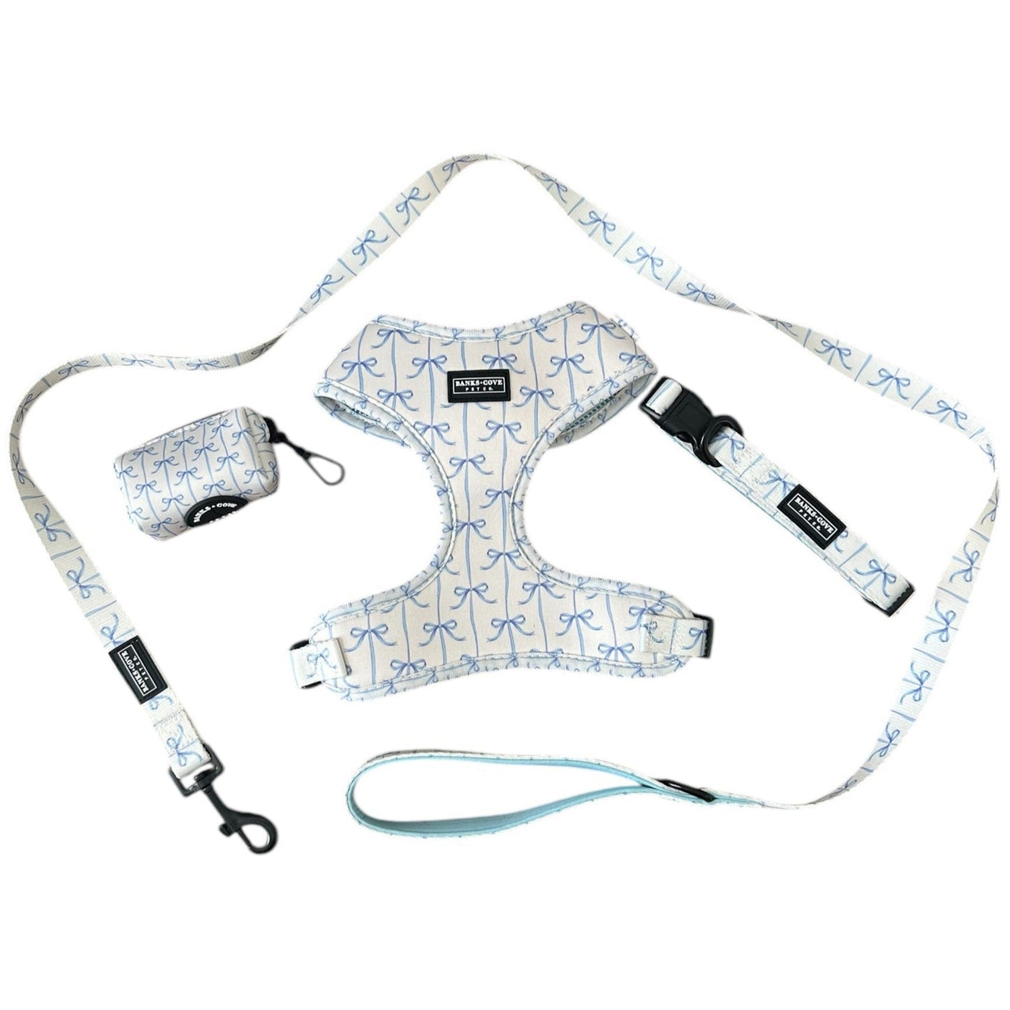 The Banks + Cove Distinguished Gentlepup 4 Piece Bundle Set features a high-quality dog harness, leash, and pouch adorned with light blue bows. Black buckles and clips provide fastening for a stylish pup.