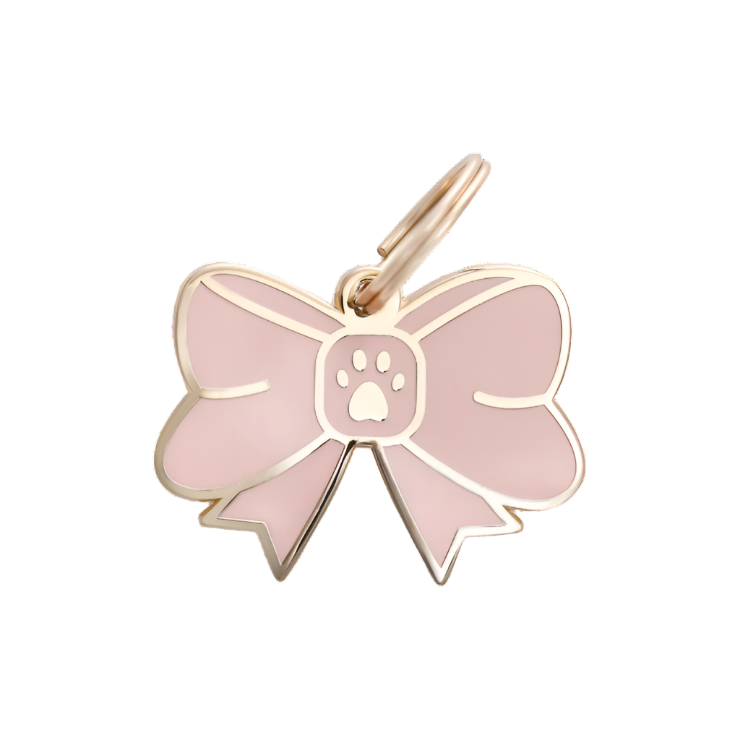 The Bow Collar Charm by Two Tails Pet Company features a gold frame and pink, bow-shaped design with a paw print center. Its designed as a pet accessory with an attached loop for easy hanging.