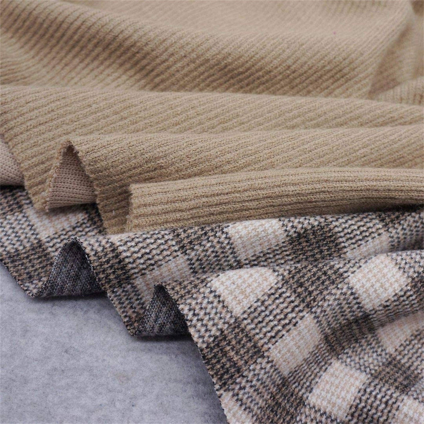 Two fabrics folded side by side on a gray surface: one is plain beige with an elastic ribbing texture, and the other showcases the Fitwarm Plaid Sweater Hoodie pattern in shades of brown, beige, and cream.