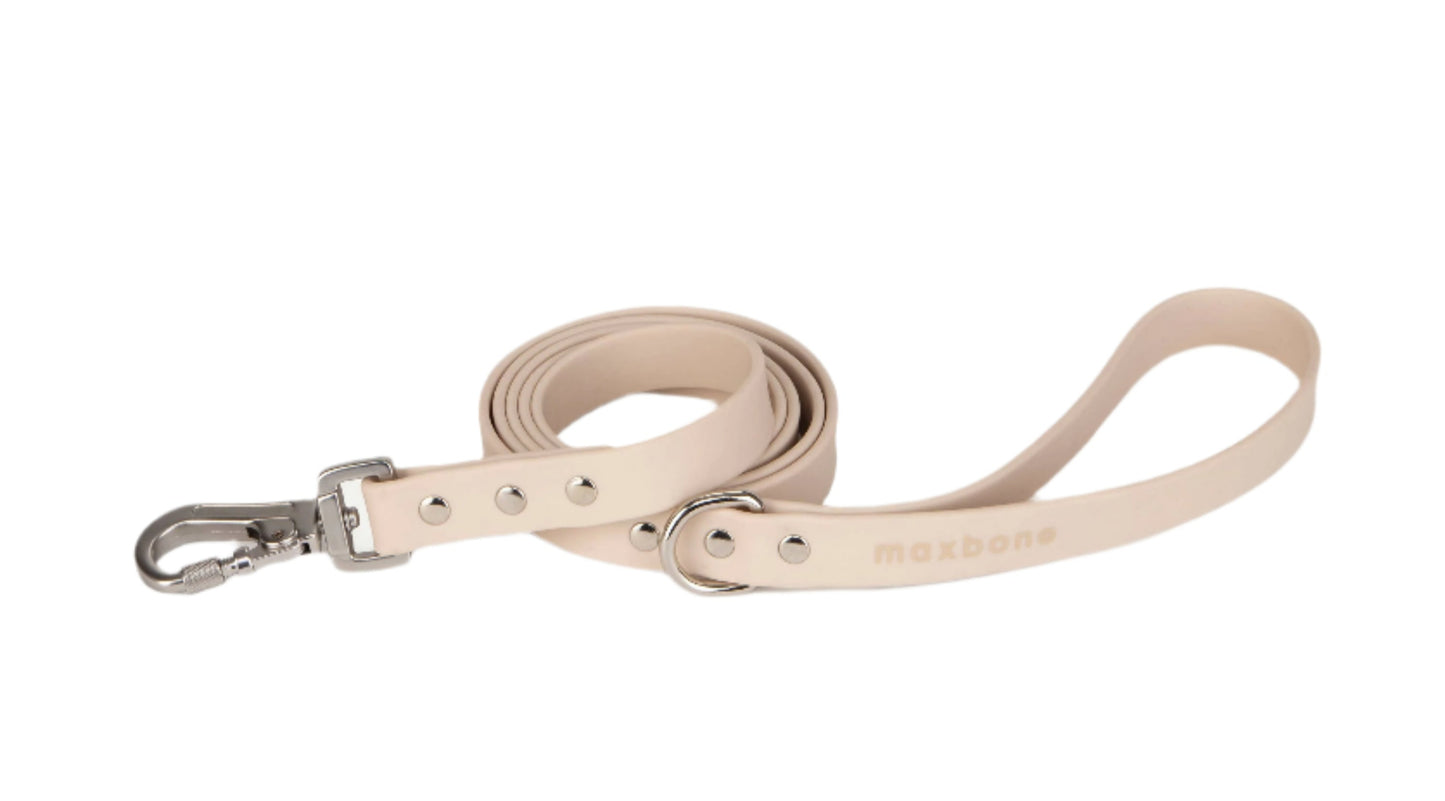 The Hazel Dog Leash by maxbone is a rolled-up beige leash made of durable webbing, featuring a metal buckle and clasp with sleek zinc alloy hardware and an embossed brand name.