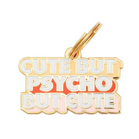 The Two Tails Pet Company offers a gold enamel keychain, cleverly doubling as the Cute But Psycho Collar Charm, featuring CUTE BUT PSYCHO BUT CUTE in vibrant white, red, and pink hues—an eye-catching accessory for you or your dog.