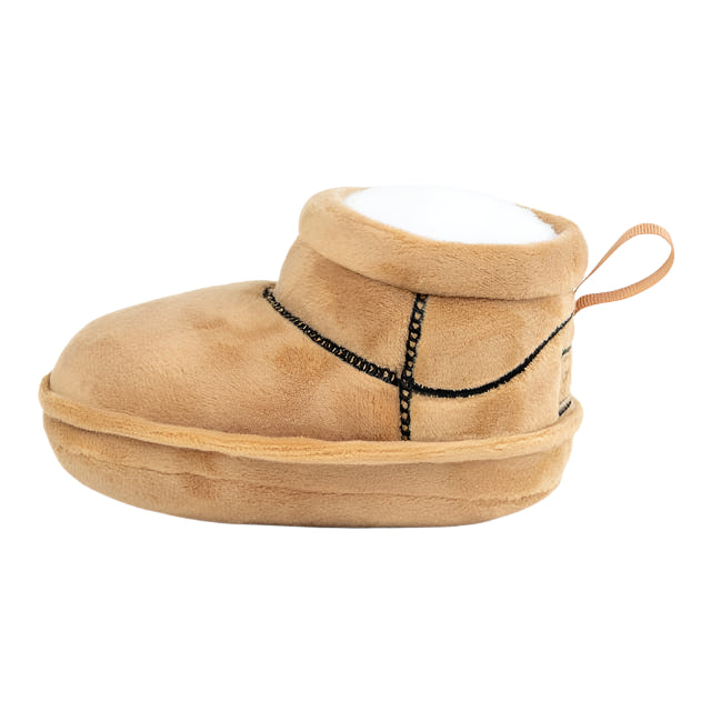 The image presents Muttzies PUGG Boot Dog Toy, a plush, tan slipper with black stitching. It has a rounded toe, soft sole, loop for easy wearing, and built-in squeaker for pet fun.