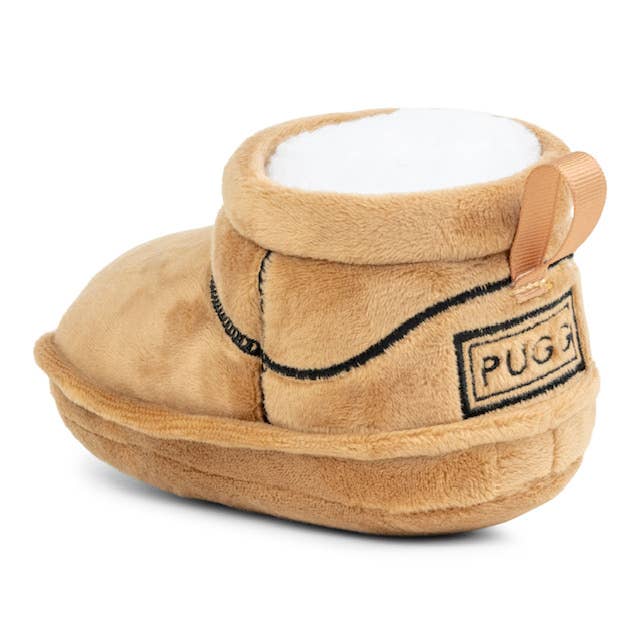 The Muttzie PUGG Boot Dog Toy is a tan-colored plush mini boot with a soft white interior, loop handle, and stitched PUGG emblem on the heel. It includes a squeaker for your pets endless entertainment.