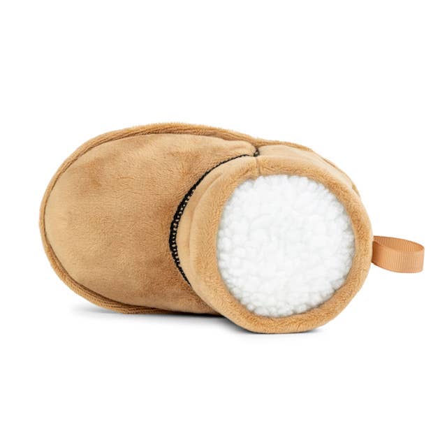 The Muttzie PUGG Boot Dog Toy features a soft, white interior, built-in squeaker, and a small loop handle on the side; its plush material and cozy design make it perfect for playful pups.