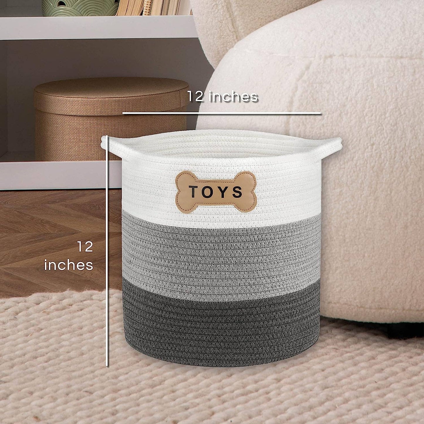 The Livra Pet Toy Basket by Park Life Designs is a cylindrical woven basket made from natural organic cotton, featuring TOYS in white, gray, and dark gray layers with a bone-shaped tag. Measuring 12x12 inches, its ideal for pet toys on a light rug near a beige couch and shelf.