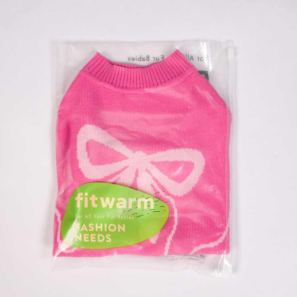 A Fitwarm Bowknot Dog Sweater in pink, featuring a cozy circular neckline and white bowknot pattern, is packaged in a clear plastic bag. The label states fitwarm for all your fur babies with fashion needs highlighted in green.