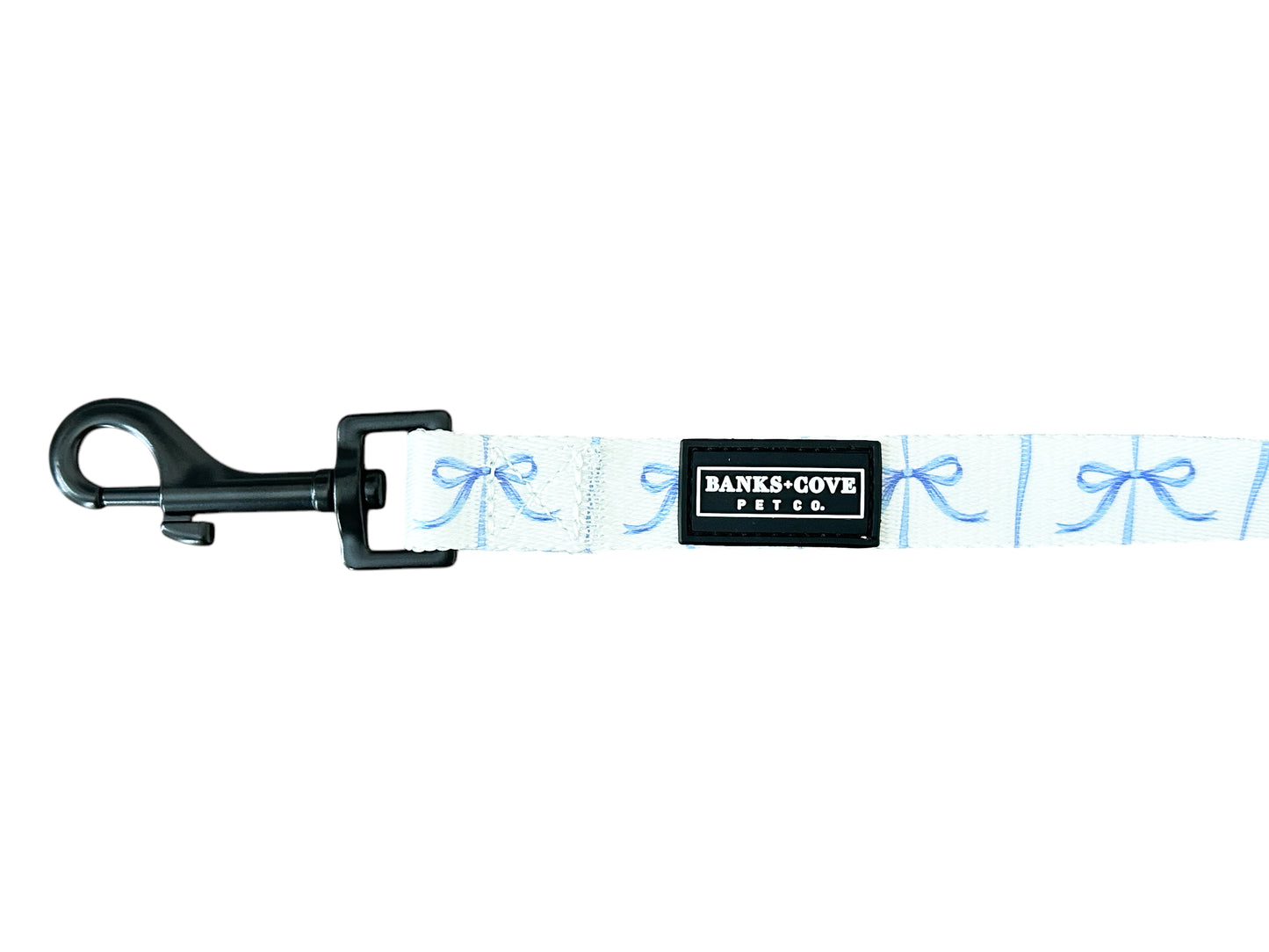 Meet the Distinguished Gentlepup Dog Leash from Banks + Cove: a light blue leash with charming bow patterns, a sturdy black clip, and a sleek black label reading Banks & Cove Pet Co, making it the ideal stylish accessory for your pampered pooch.