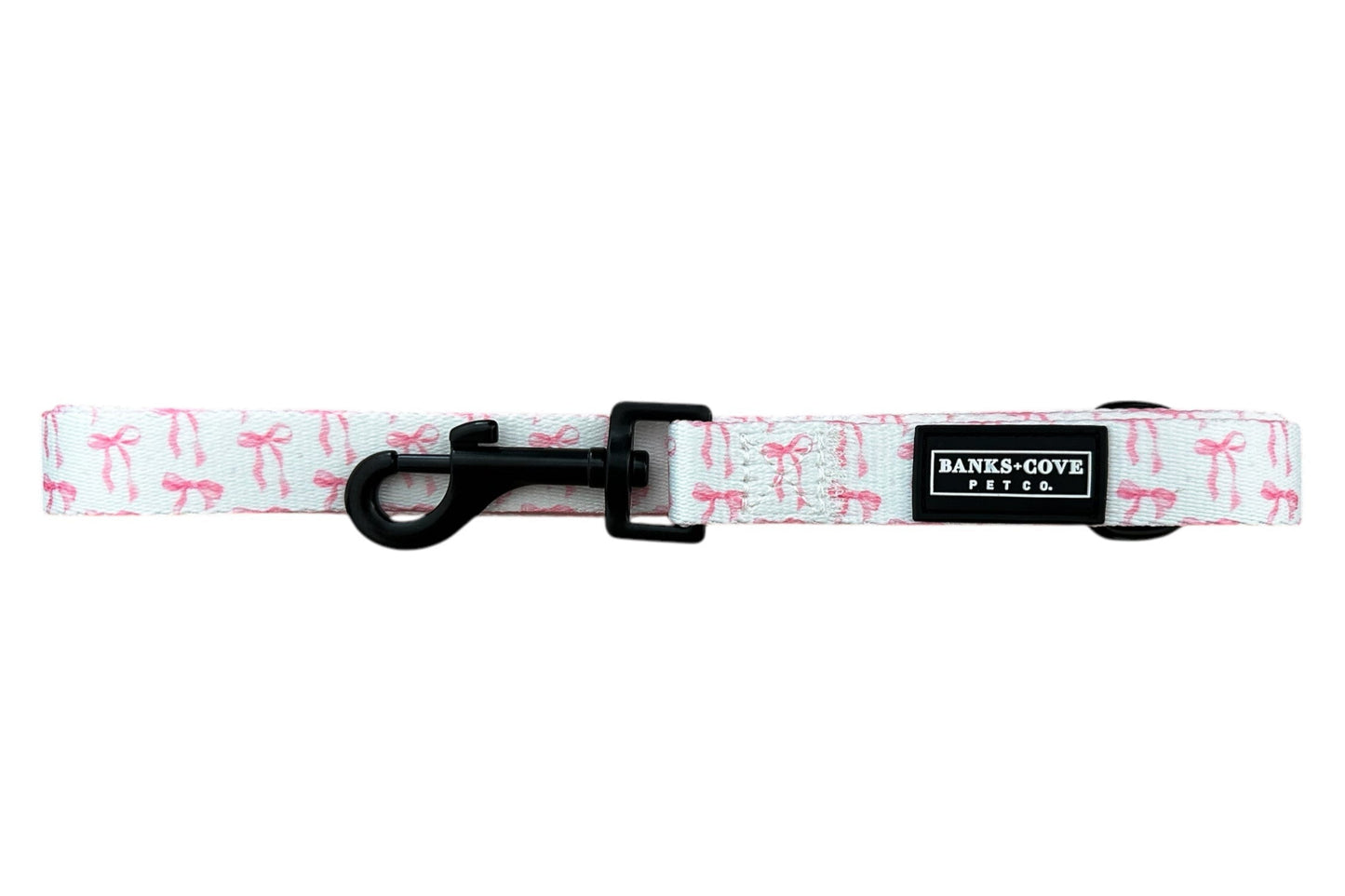 Introducing The Coquette Pooch- Dog Leash by Banks + Cove: a pink leash with bow patterns, a padded handle for comfort, and a black hook clasp. Made from durable webbing and featuring the label BANKS COVE.