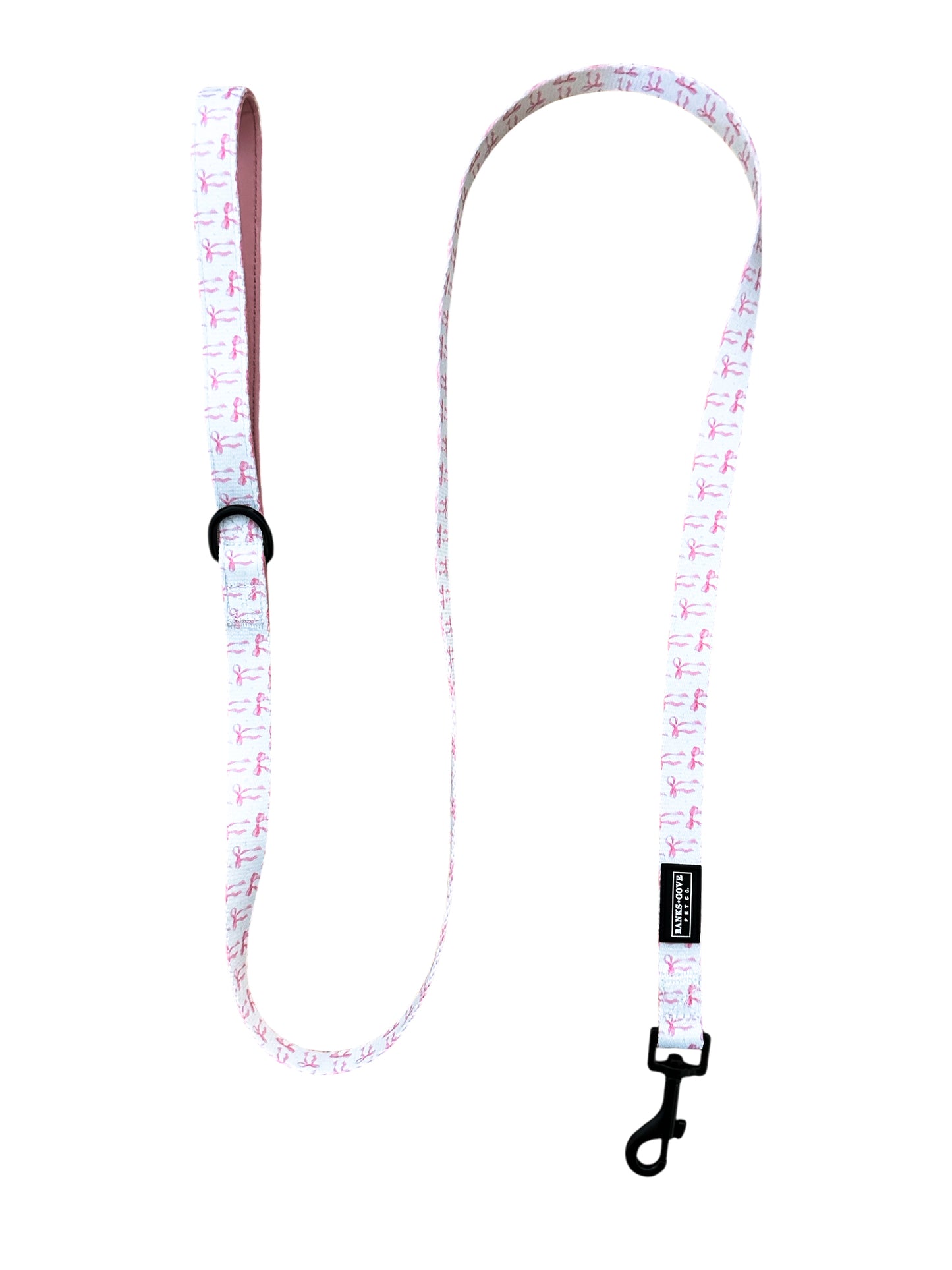 Introducing the Coquette Pooch Dog Leash by Banks + Cove: a charming white leash with pink flamingo pattern, made from durable webbing. It includes a padded handle for comfort, a black metal clasp, and an adjustable buckle for the perfect fit.
