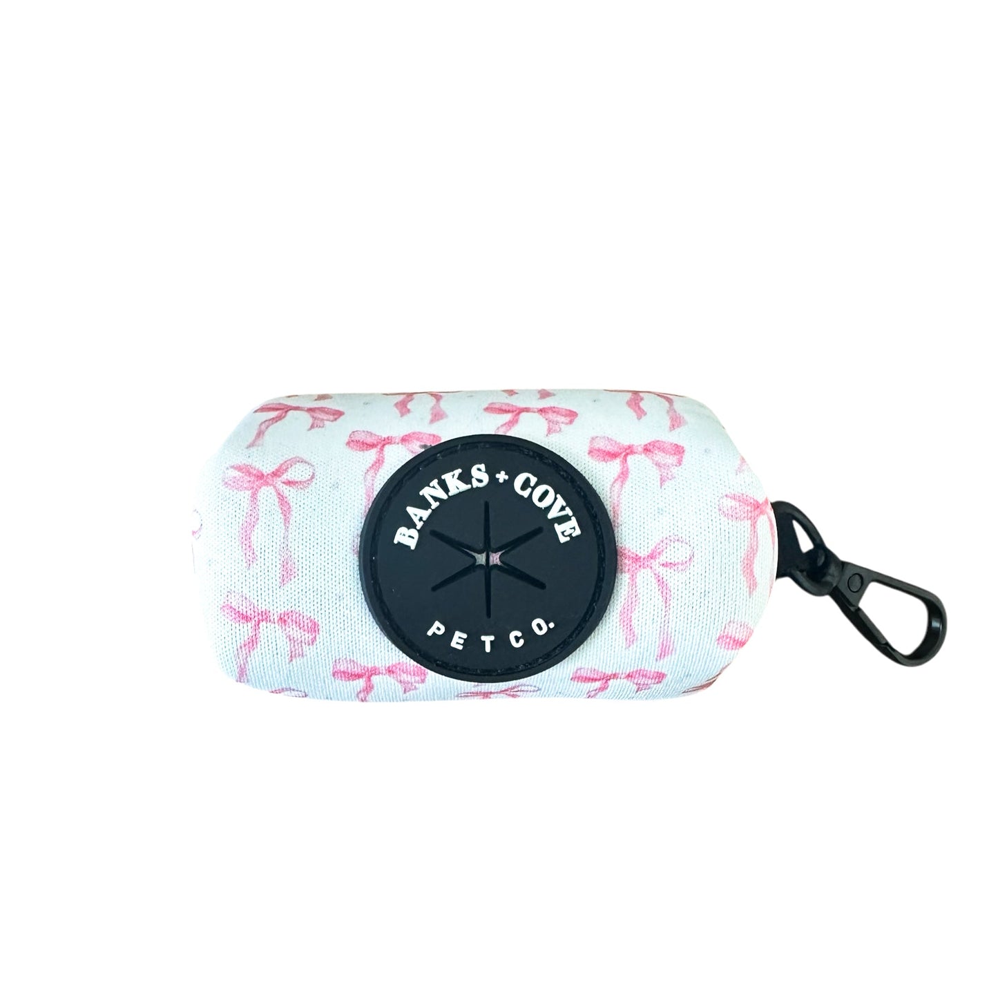 The Coquette Pooch Waste Bag Holder by Banks + Cove is a stylish white pet accessory with a black clip and circular logo. It features a pink bow pattern, making it an elegant addition to any fashionable dog accessory collection.