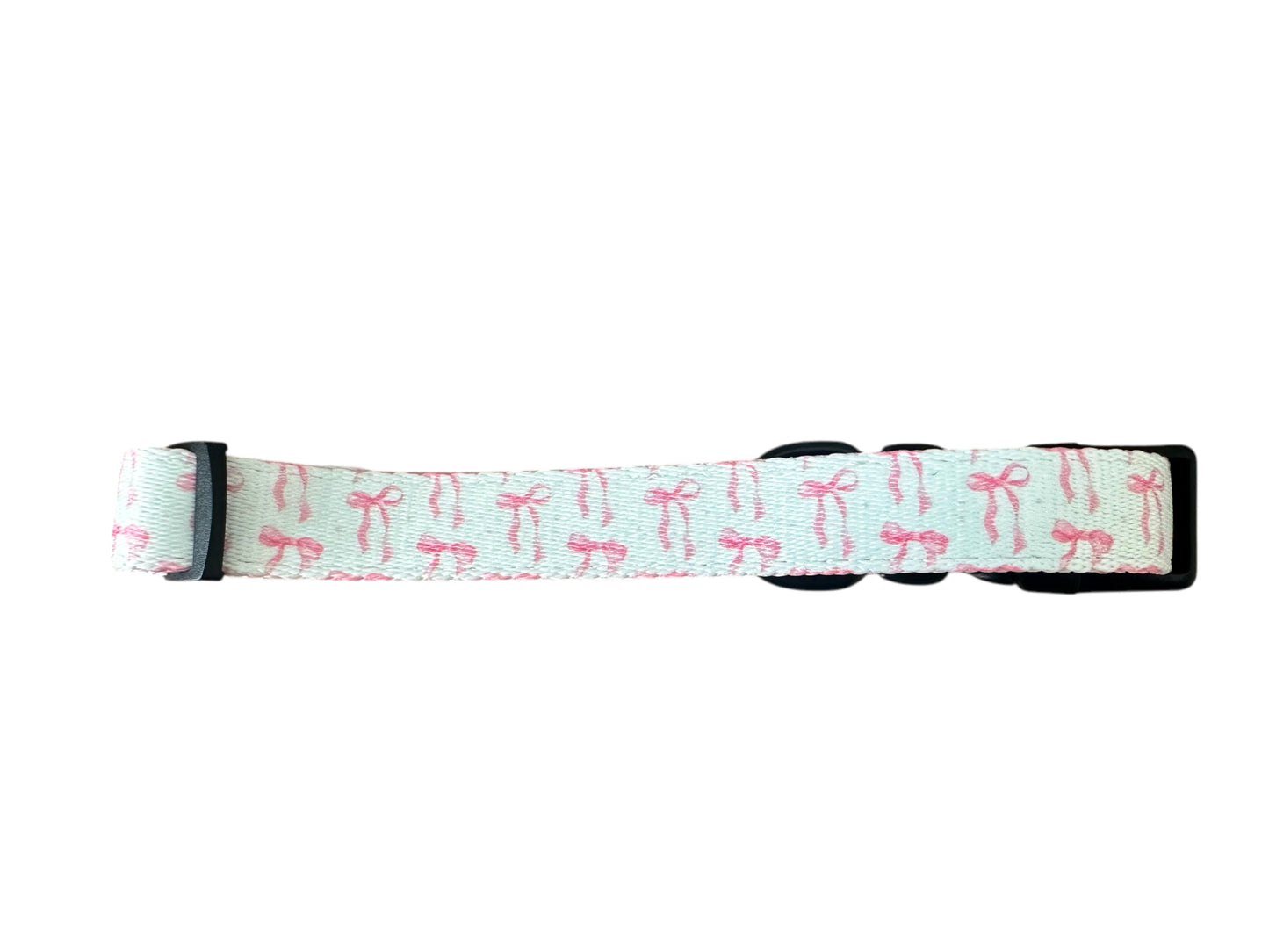 Introducing Banks + Coves The Coquette Pooch Dog Collar: a light blue collar featuring small pink bows and sleek black buckles. This stylish accessory combines elegance and charm for your beloved pet.