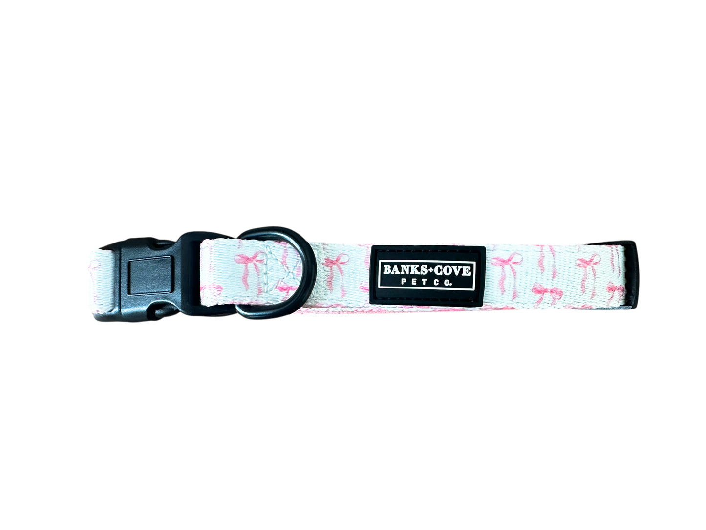 Introducing the Coquette Pooch Dog Collar: a chic accessory with a white base and pink flamingo patterns, featuring a black plastic buckle, durable metal D-ring, and an elegant Banks + Cove label.
