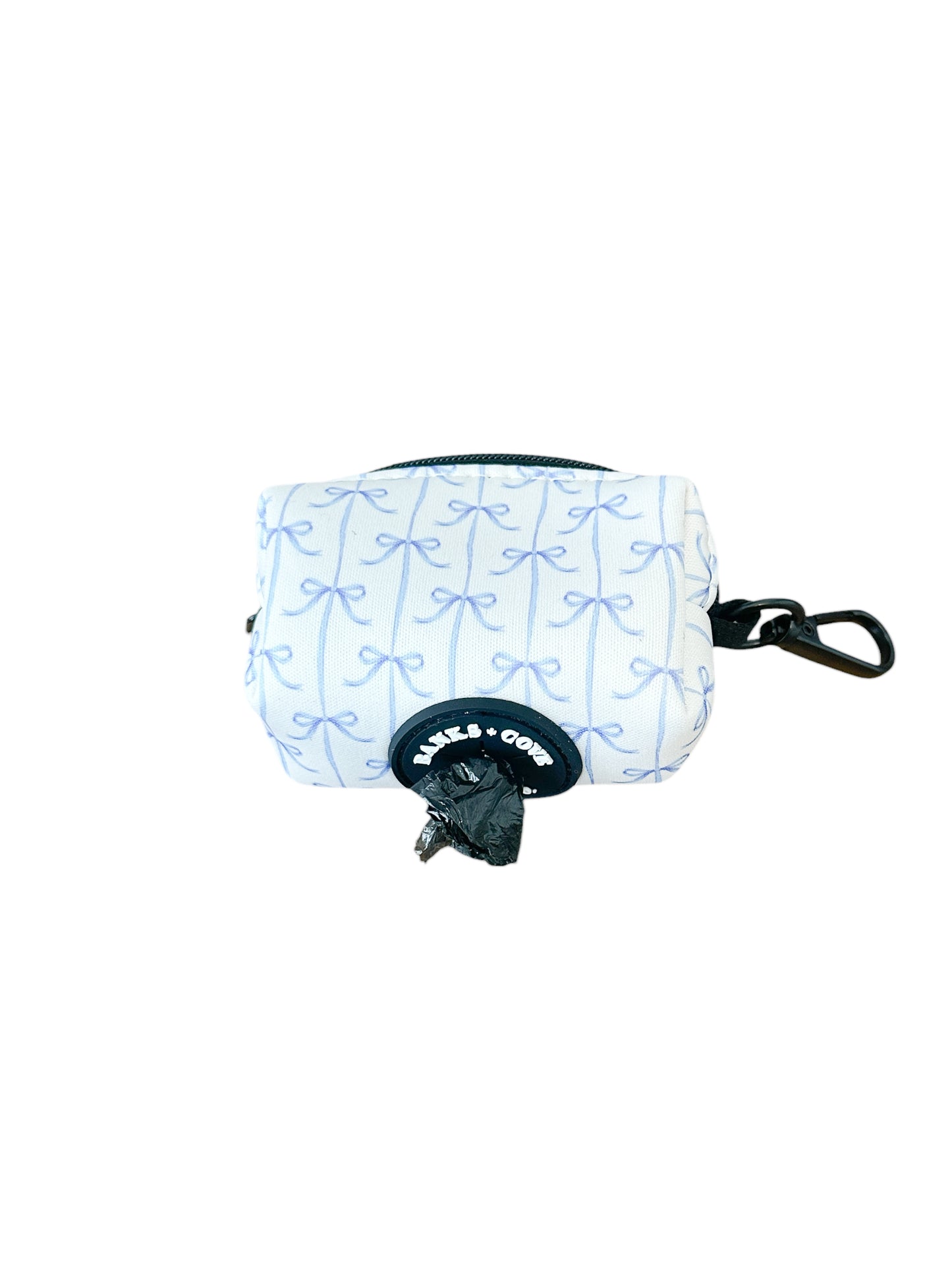The Banks + Cove Distinguished Gentlepup Waste Bag Holder is small and white, with a blue bow pattern and black zipper. It features durable fabric, a black clip for leash attachment, and dispenses black bags seamlessly from the bottom.