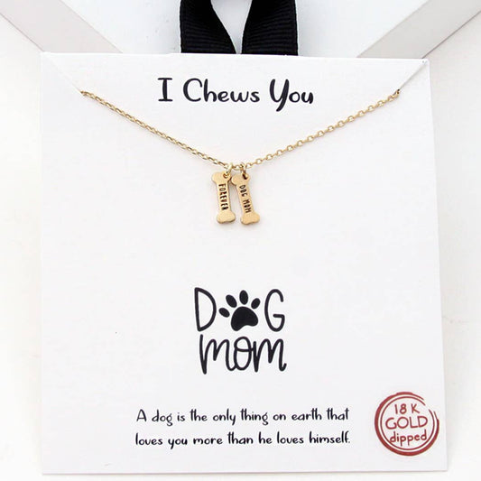 The I Chews You – Dog Mom Bone Charm Necklace by Banks + Cove features two bone-shaped pendants labeled Dog Mom with an 18K gold-dipped tag. The packaging says I Chews You and showcases a paw print, celebrating a dogs love while adding elegance to the piece.