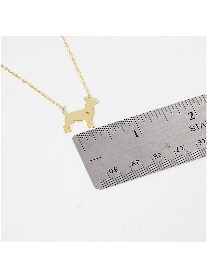 The Banks + Cove Chihuahua Love Necklace, a gold-tone piece shaped like a small dog, is shown next to a 2-inch metal ruler for scale on a white background.