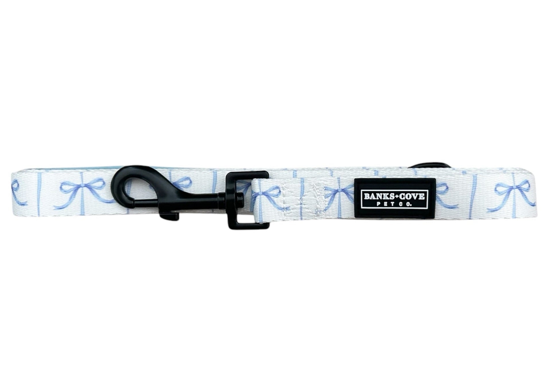 Introducing the Distinguished Gentlepup Dog Leash by Banks + Cove, a stylish white accessory with a blue bow pattern, black metal clip, and stitched logo label—perfect for elegant walks with your furry friend.